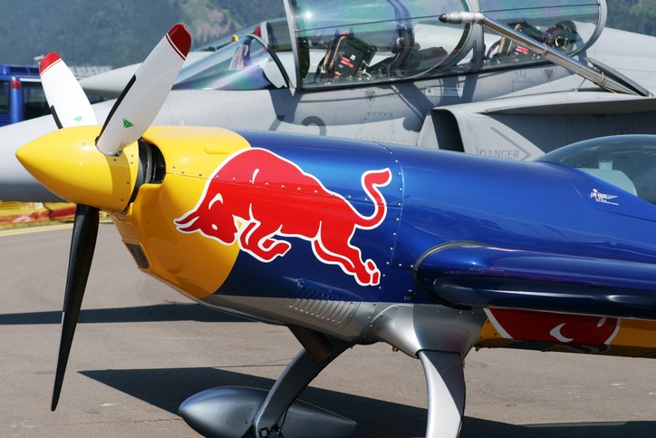 Front part of Extra 300S aerobatic plane with Red Bull sign on it on display at Airpower 11 air show. Extra 300S is one of the best aerobatic competition aircraft designed by Walter Extra from Germany. In the background canopy of fighter airplane Saab JAS 39 Gripen is visible.